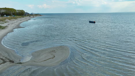 Aerial-view-of-a-coastal-landscape-featuring-a-solitary-boat-on-calm-waters-near-a-sinuous-sandbar,-capturing-the-serene-interaction-between-sea-and-shore