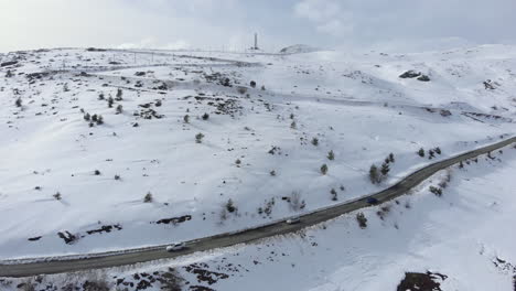 Drone-view-of-cars-passing-crossing-high-altitude-mountain-road-beautiful-slopes-covered-in-snow-winter-day