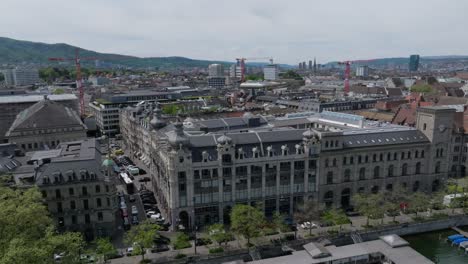 Panning-drone-shot-of-Zurich-city,-showing-old-town-architecture,-clock-towers-and-cities-skyline-with-river-in-the-foreground