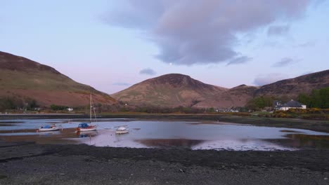 View-overlooking-calm,-shallow-ocean-water-with-moored-sail-boats-and-a-stunning-mountainous-backdrop-on-the-Isle-of-Arran,-Western-Scotland-UK