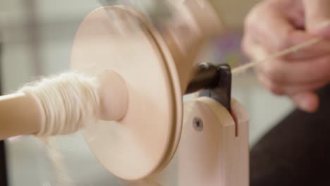 Craft-artisan-hands-feed-wool-into-spinning-wheel-to-make-yarn-closeup
