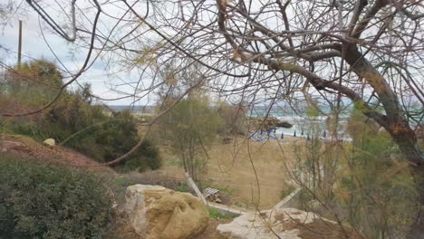 View-from-above-a-rocky-coastal-area-leading-into-a-turquoise-sea,-framed-by-sparse-vegetation-and-a-clear-sky