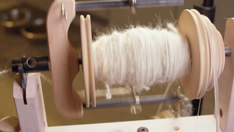 Scratchy-wool-yarn-spins-rolls-onto-spinning-wheel-bobbin,-close-up