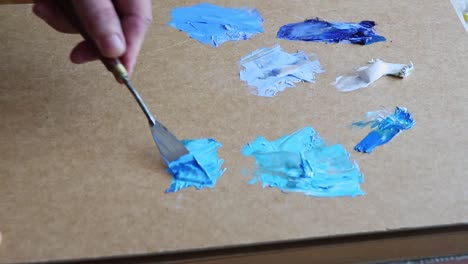 Hand-with-oil-painting-mixing-tool-blends-blue-colour-hues,-close-up