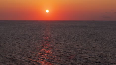 Aerial-orbit-parallax-showcases-hazey-orange-red-gradient-fire-sunset-above-serene-Caribbean-sea