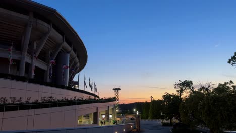 Exterior-Del-Estadio-Al-Atardecer,-Cielo-Despejado-Y-Banderas-Ondeando,-Un-Entorno-De-Arquitectura-Urbana-Moderna