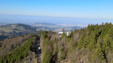 Weißer-Camper-Van-Fährt-Auf-Einer-Bergstraße-Mit-Der-Stadt-Freiburg-Im-Breisgau-Im-Hintergrund-Sichtbar