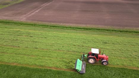 Eine-Drohne-Dreht-Sich-über-Einem-Landwirt,-Der-Mit-Einem-Mähbalken-Auf-Seinem-Traktor-Sitzt-Und-Das-Gras-Auf-Seiner-Weide-Mäht