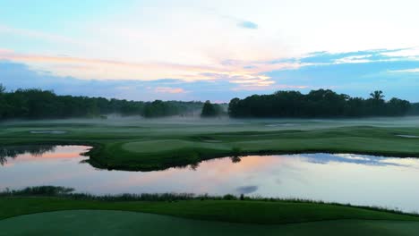 Sobrevuelo-En-Un-Campo-De-Golf-Con-Una-Impresionante-Muestra-De-Niebla-Que-Lentamente-Sale-De-La-Línea-Del-Bosque