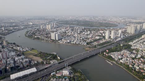 Ho-Chi-Minh,-Saigon,-Vietnam,-with-the-river-flowing-between-the-residential-areas-and-a-bridge,-aerial-drone-video-during-sunset