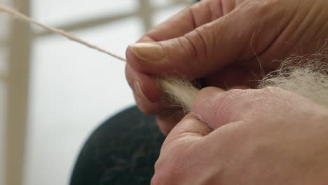 Closeup-hands-pull-natural-wool-into-spinning-wheel,-making-grey-yarn