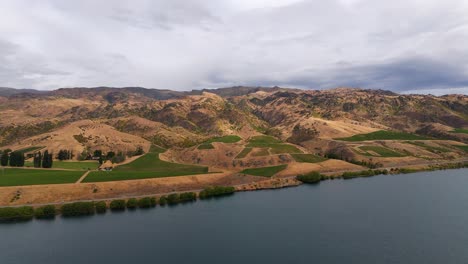 Central-Otago-region-hills-and-valleys-slope-down-to-Lake-Dunstan-New-Zealand,-aerial