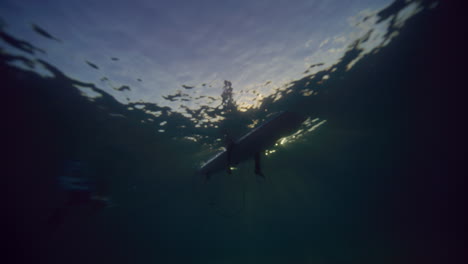 Underwater-view-looking-up-at-surfer-sitting-on-longboard