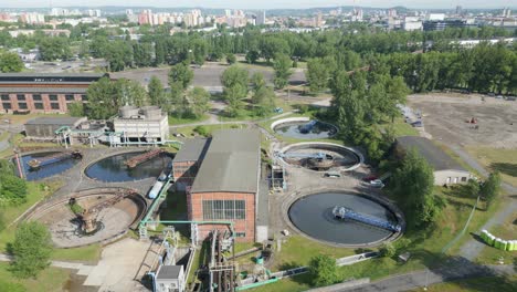 aerial-view-of-a-wastewater-treatment-plant,-featuring-multiple-circular-tanks-amidst-greenery-and-urban-structures
