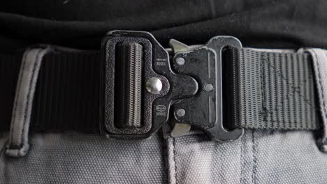 Close-up-of-a-man-unbuckling-a-tactical-black-belt-from-his-trousers