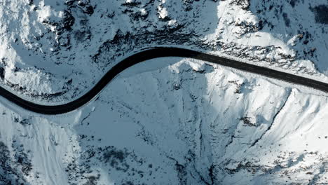 Un-Camino-Sinuoso-Que-Atraviesa-Un-Paisaje-Montañoso-Cubierto-De-Nieve,-Capturado-A-La-Luz-Del-Día,-Vista-Aérea