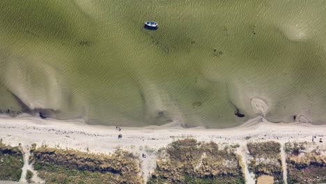 An-aerial-view-of-a-lone-boat-anchored-near-a-sandy-beach,-with-clear-shallow-water-revealing-the-seabed-patterns-and-sparse-underwater-vegetation