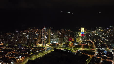 Toma-Aérea-De-Seguimiento-De-Rascacielos-Iluminados-Por-La-Noche-En-El-Centro-De-Bogotá,-Colombia.