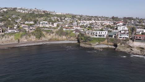 Aerial-track-right-to-left-of-hmes-on-an-oceanside-cliff-in-San-Diego,-California-with-a-rocky-beach-on-a-sunny-day