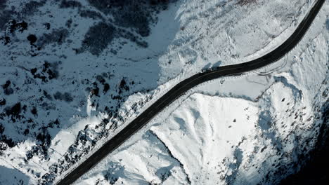 Winding-road-through-a-snow-covered-mountain-landscape,-aerial-view