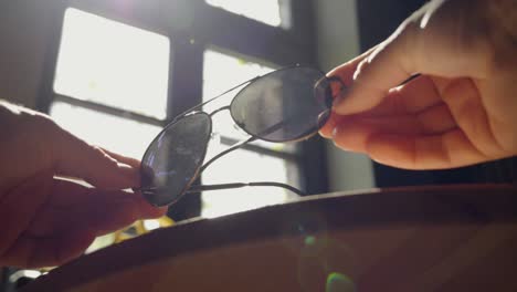 Sonnenbrille-Vor-Dem-Hintergrund-Des-Sonnenlichts,-Das-Durch-Ein-Holzfenster-Strömt