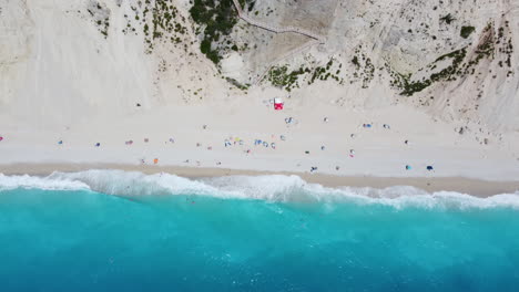 Waves-crash-along-the-Greek-shoreline,-where-white-sand-and-crystal-clear-blue-water-meet