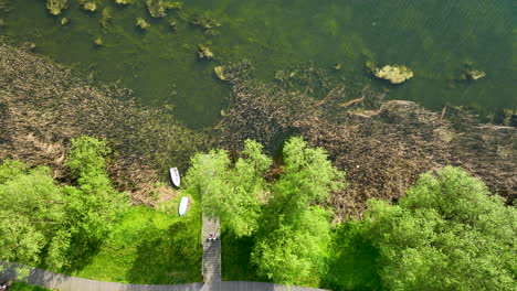 Vista-Aérea-De-Una-Serena-Escena-Fluvial-Con-Exuberantes-Orillas-Verdes-Y-Pequeñas-Embarcaciones-Atracadas-A-Lo-Largo-De-Un-Estrecho-Muelle