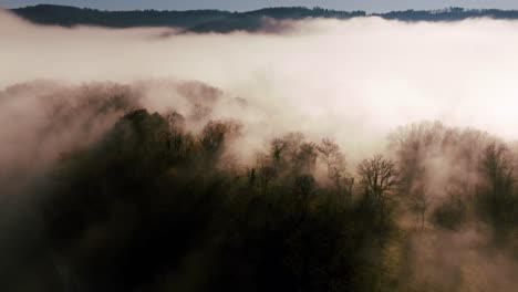 Dive-into-the-mist-over-a-forest-with-a-drone,-morning-in-the-Dordogne-above-a-cliff