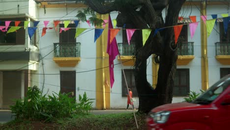 Colorful-flags-hung-on-tree-in-urban-setting-with-person-walking,-warm-daylight