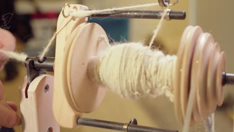 Closeup-artisan-uses-tool-to-load-spinning-wheel-bobbin-with-wool-yarn