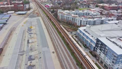 Aerial-of-a-metro-crossing-through-Atlanta-BeltLines-massive-shipping-facility-towards-King-Memorial-subway-station-with-the-view-of-Downtown-Atlanta-buildings-in-background,-Georgia,-USA