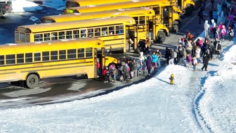 Elementary-school-children-boarding-yellow-school-buses-to-go-home-on-snow-day,-early-dismissal,-two-hour-delay