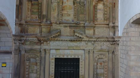 Ascending-flight-with-a-drone-visualizing-the-entrance-porch-of-the-church-of-San-Vicente,-exploring-its-magnificent-baroque-style-stone-decoration,-we-see-the-entrance-vault-and-roof