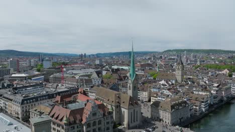 Fast-ascending-drone-shot-showing-city-inhabitants,-the-clock-towers,-public-transport-and-skyline-of-Zurich