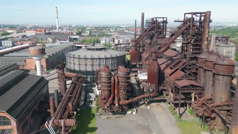 Luftaufnahme-Einer-Verrosteten-Industrieanlage,-Gegenübergestellt-Vor-Einer-Modernen-Stadtlandschaft-Unter-Klarem-Himmel