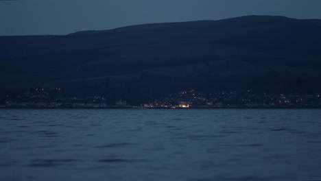 Coastal-lights-of-town-below-hillside-on-water's-edge-at-blue-hour