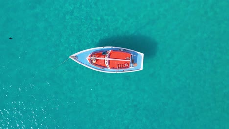 Velero-Naranja-Con-Cubierta-Azul-Anclado-En-Aguas-Turquesas-Del-Océano-Caribeño,-Descenso-De-Drones