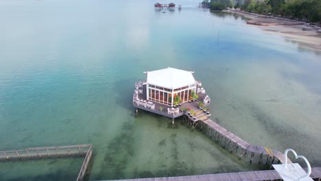 Toma-Aérea-De-Un-Restaurante-Flotante-Con-Un-Muelle-De-Madera-En-Medio-Del-Mar