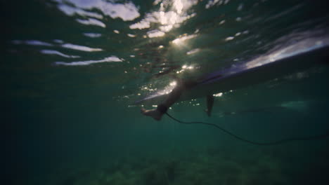 Person-sits-on-front-of-longboard-kicking-legs-underwater-with-light-ray