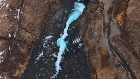 Aerial-shot-of-the-stunning-Bruarfoss-waterfall-in-Iceland,-showcasing-vibrant-blue-waters-weaving-through-dark-rocks