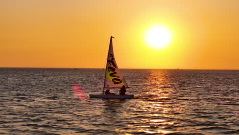 Small-Dinghy-Training-Sailboat-Isolated-On-A-Beautiful-Sunset-Sea