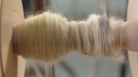 Close-up-craft-detail:-Wool-yarn-spools-onto-spinning-wheel-bobbin