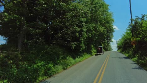 Eine-Ruhige-Fahrt-Entlang-Einer-Grünen-Landstraße-Unter-Klarem,-Blauem-Himmel,-Während-Man-An-Einem-Pferdewagen-Der-Amischen-Vorbeifährt