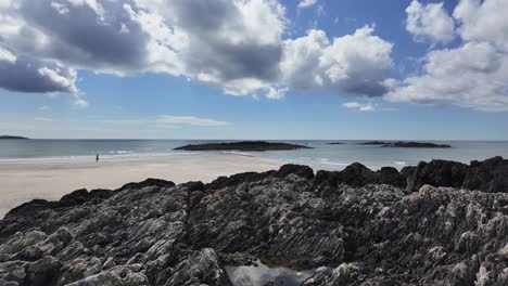 Dark-rocks-and-sand-contrast-the-blue-sky-and-white-clouds-on-the-Owenahincha-beach-in-West-Cork,-Ireland