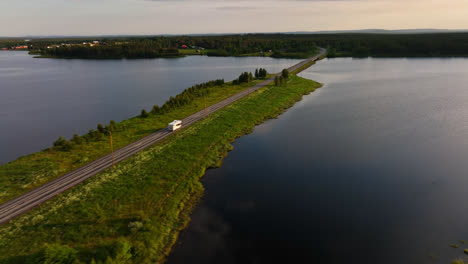 Drones-Rastreando-Una-Caravana-Conduciendo-En-Medio-De-Lagos-De-Laponia,-Puesta-De-Sol-De-Verano