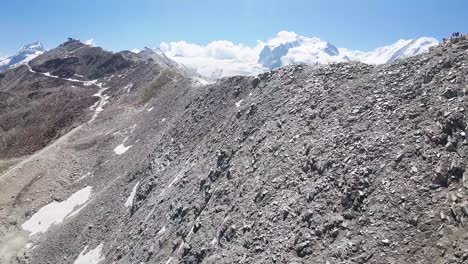 Flight-over-a-hiking-trail-at-Alps-mountains-in-Gornergrat,-Zermatt,-in-Switzerland-with-the-reveal-view-of-a-beautiful-glacier