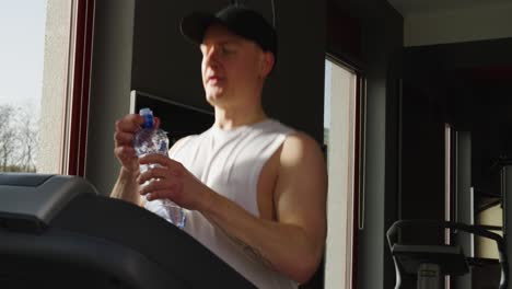 Male-athlete-run-on-treadmill-and-drink-water-from-sport-bottle,-indoor-gym