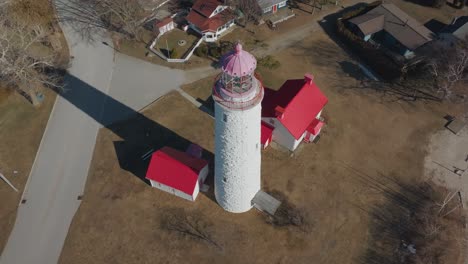 A-traditional-lighthouse-with-red-roofs-during-the-day,-showing-surrounding-paths-and-sparse-trees,-aerial-view