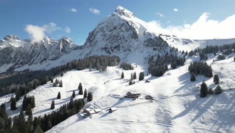 Aerial-drone-backward-moving-shot-over-snow-covered-mountain-range-in-Fronalpstock-Switzerland-Glarus-on-a-cold-winter-day