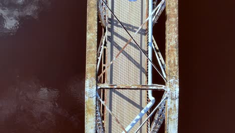 Two-people-crossing-a-metallic-bridge-above-the-water-Aerial-Top-Down-View